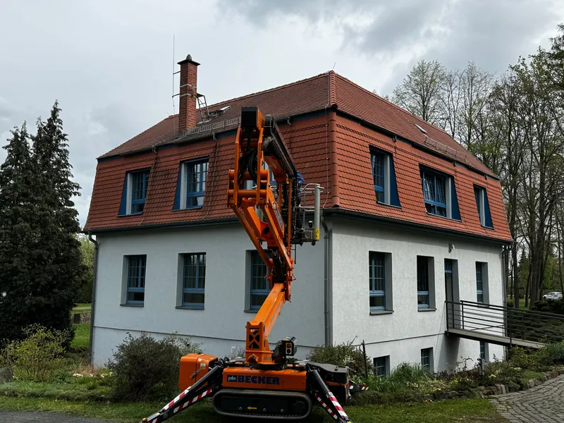 Mehrfamilienhaus mit Ziegeldach, davor eine Arbeitsbühne für den Fassadenanstrich