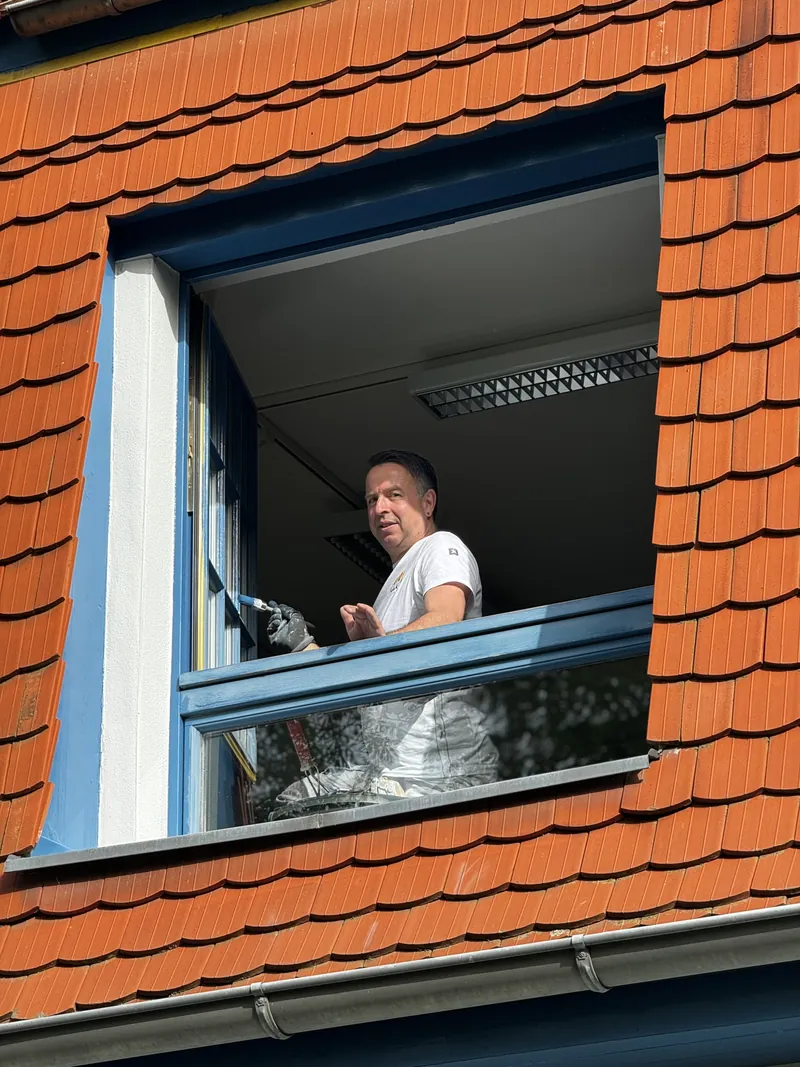 Maler bearbeitet ein Dachgaubenfenster von innen