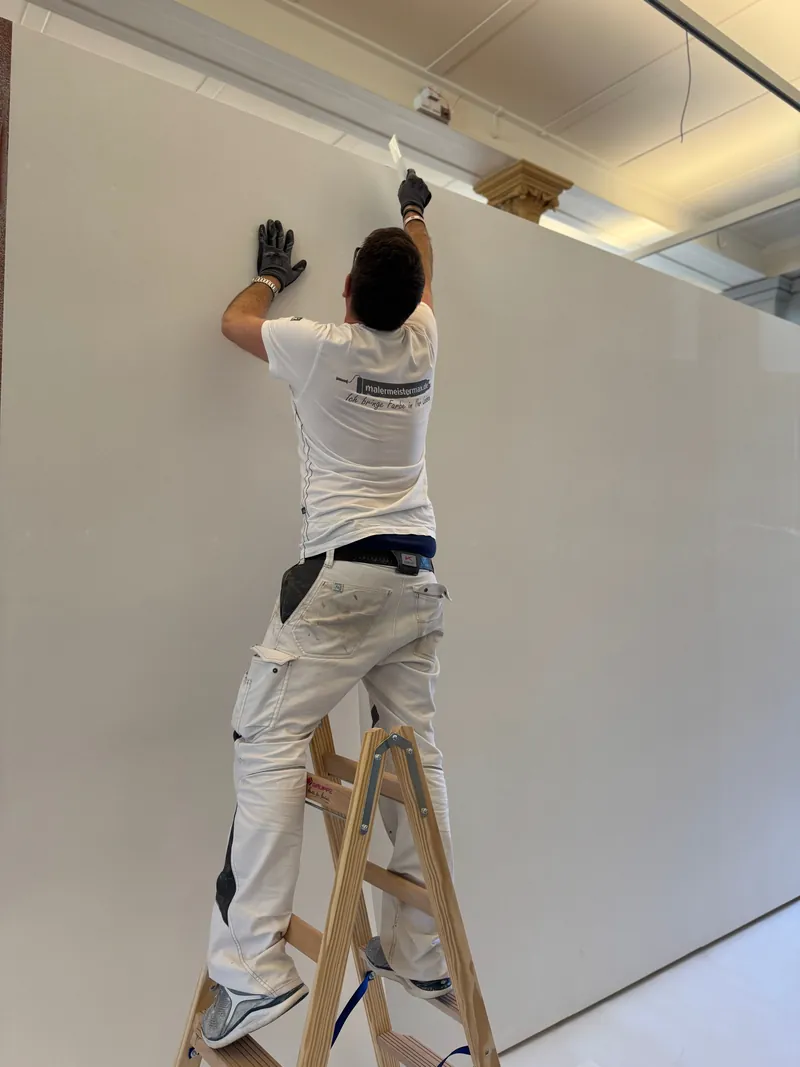 Maler streicht auf der Leiter eine Wand weiß