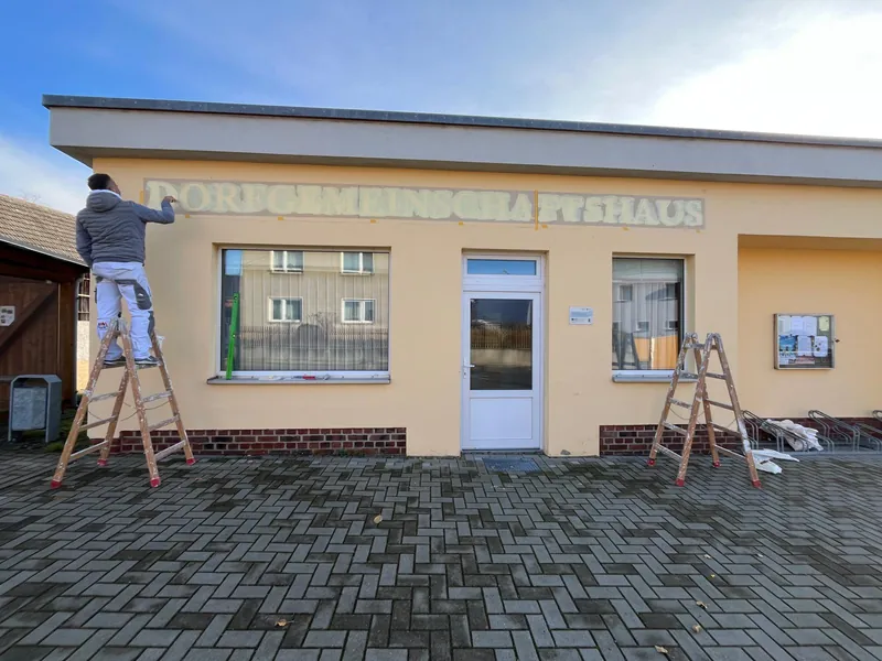 Maler auf der Leiter bei der Beschriftung des Dorfgemeinschaftshauses