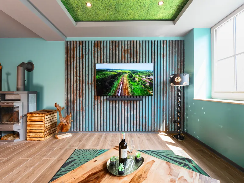 Wohnzimmer mit Lamellenwand, Fernseher und Decke im Moos-Look