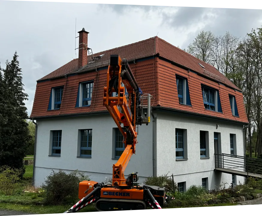 Mehrfamilienhaus mit Ziegeldach, davor eine Arbeitsbühne für den Fassadenanstrich