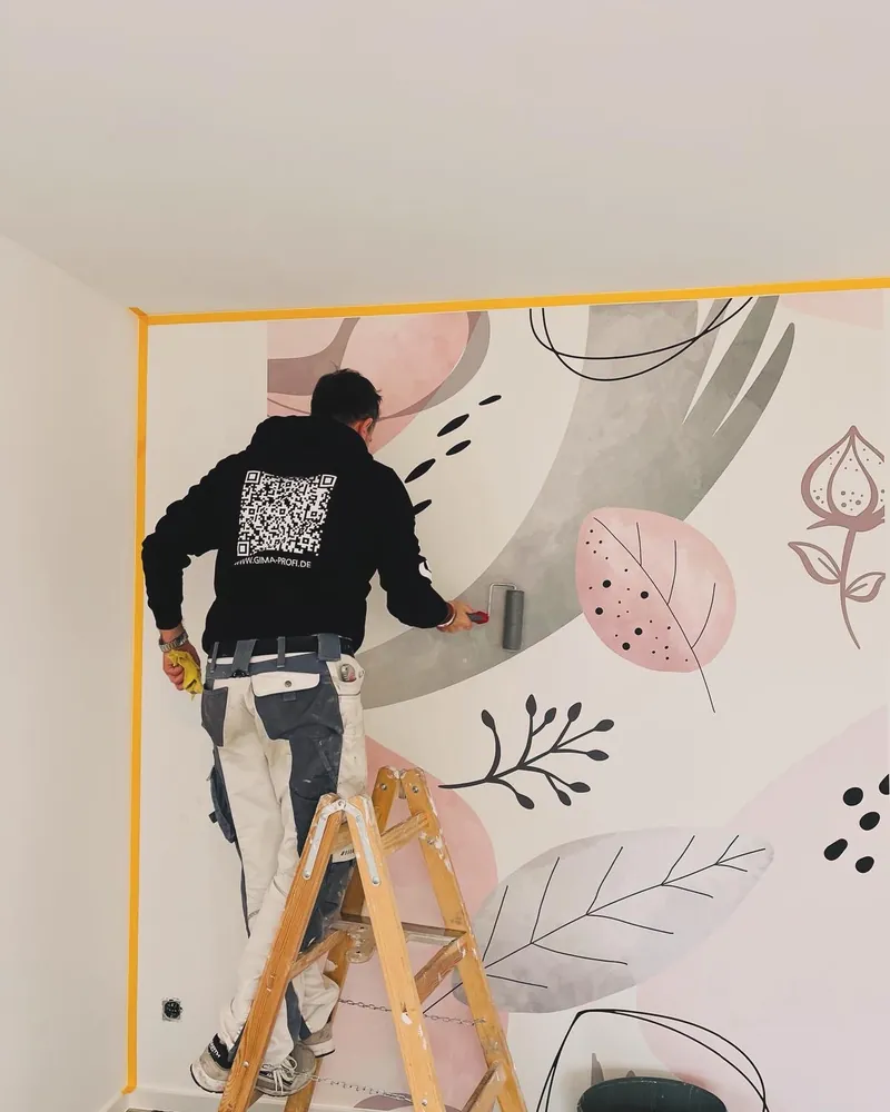 Maler auf der Leiter bringt eine Wandtapete mit Blattmotiven an