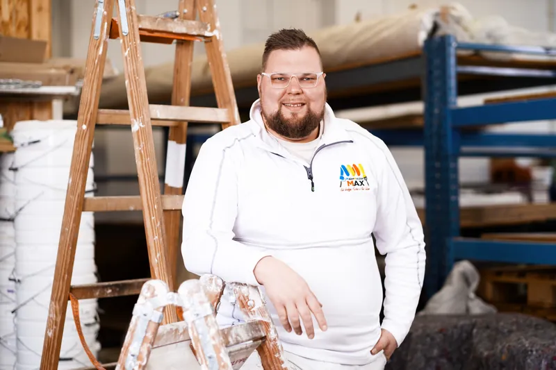 Maximilian Petzold, Malermeister und Inhaber, sitzt auf einer Leiter in der Werkstatt